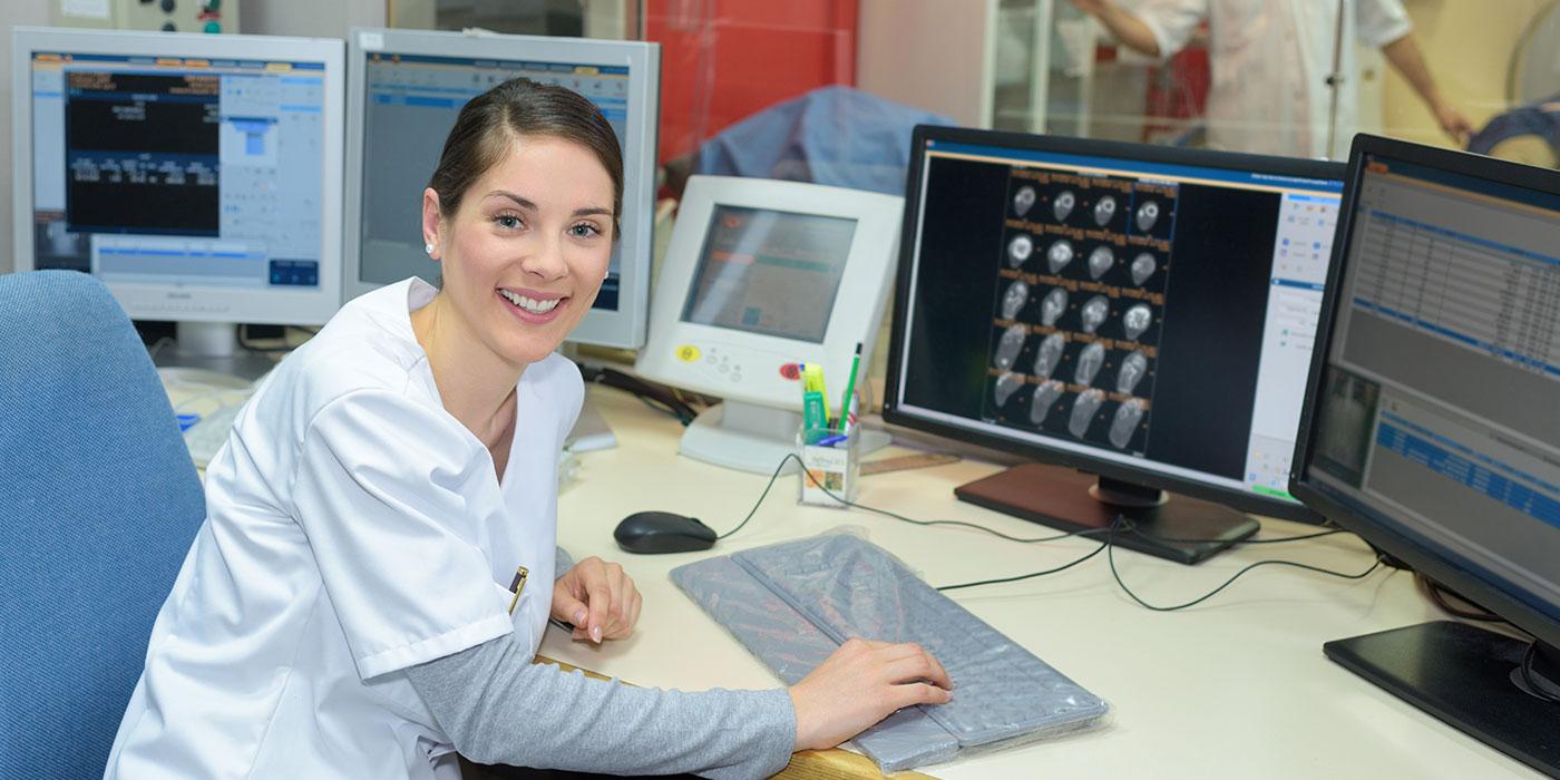 Woman in scrubs sitting at a computer with brain scans on the moniter.